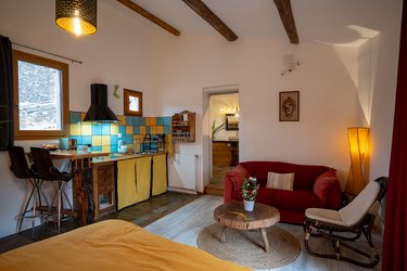 Studio sous poutres apparentes avec lit à couette jaune moutarde, table basse en bois brut et coin cuisine
